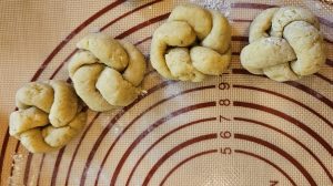 Four balls of dough formed into double knots lying on a pastry mat.