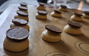 Baking tray with multiple cookie dough shapes topped with chocolate discs on a silicone mat.
