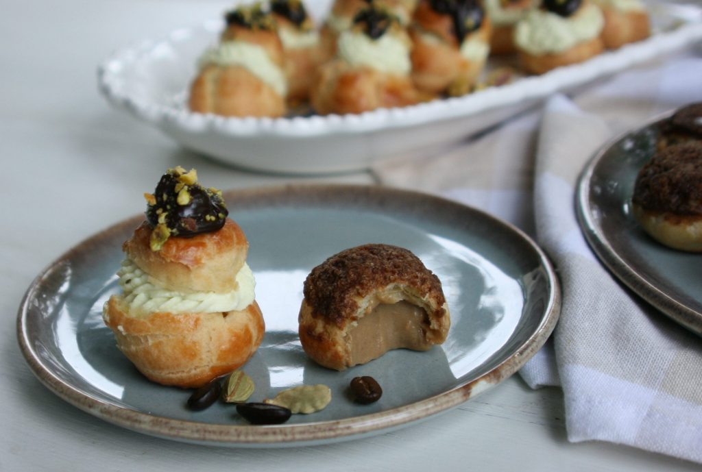 A plate with two pastries: one layered with cream and topped with chocolate and nuts, and the other partially bitten, revealing a creamy filling inside.